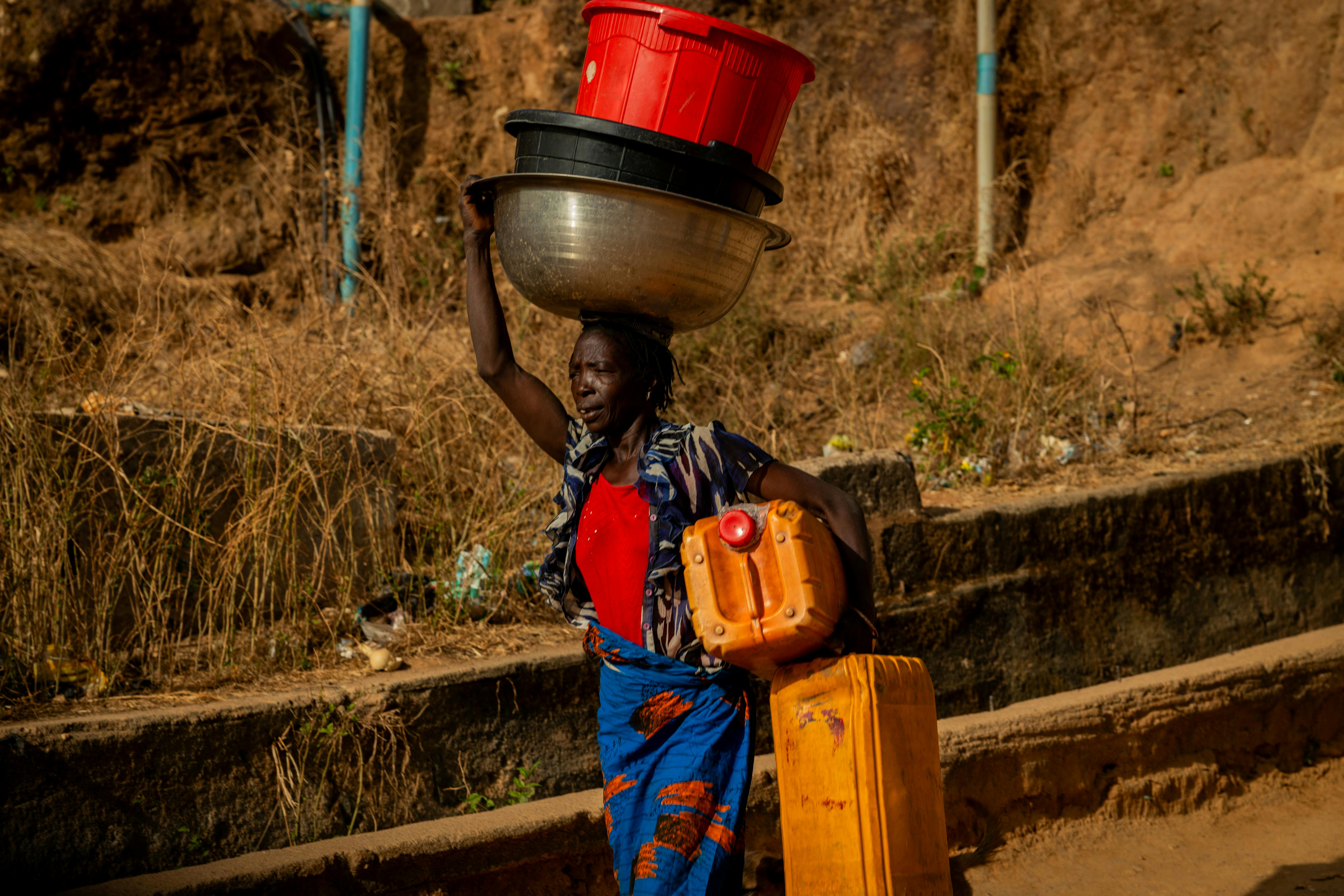 A woman carrying water containers in a dry, arid setting in Sub-Saharan Africa